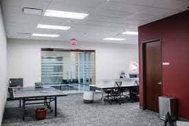 Modern office space with maroon walls, several desks, chairs, and computers; a glass-walled meeting room is visible in the background.