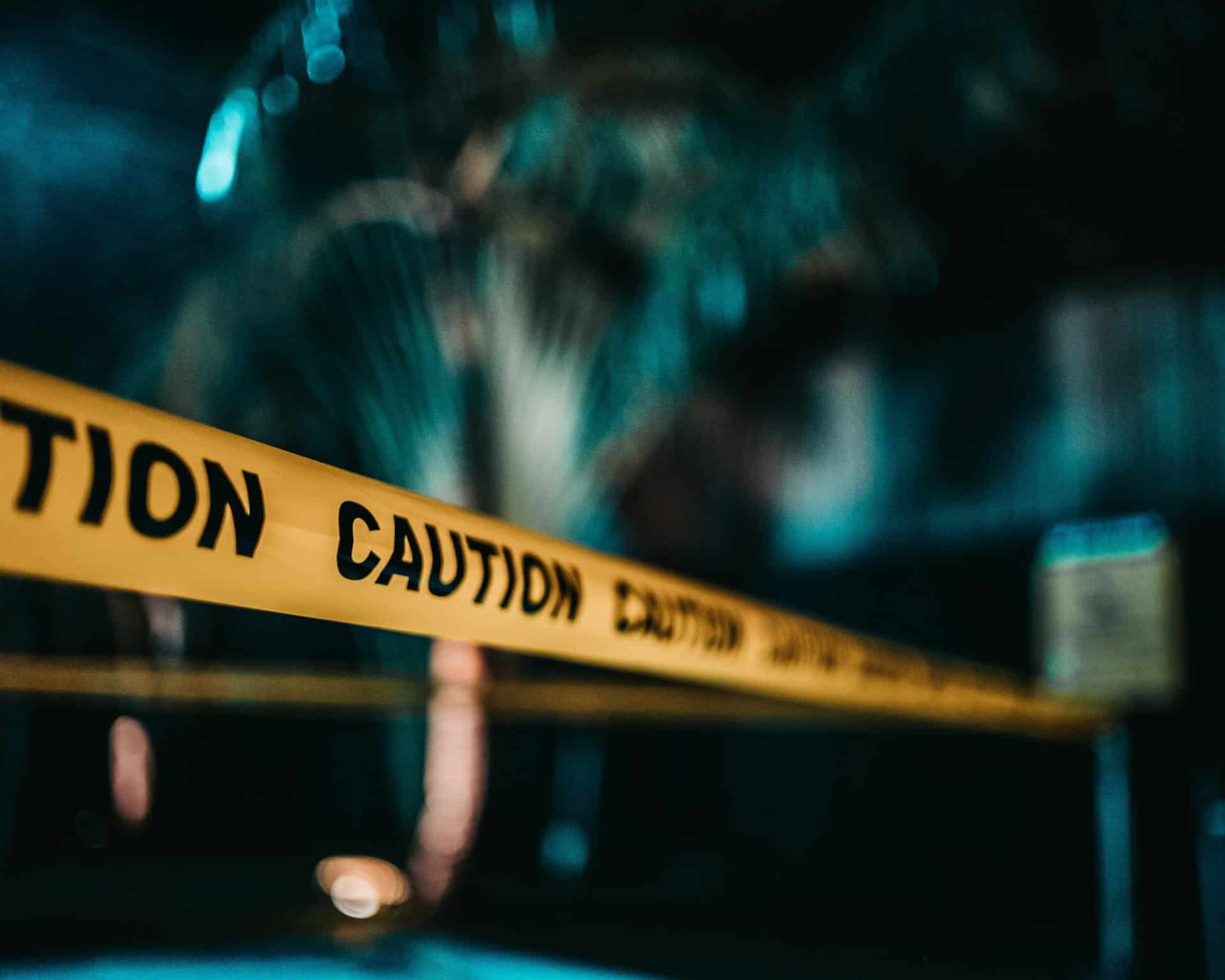 Yellow caution tape is stretched across an area, with an out-of-focus background featuring trees.