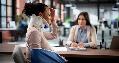 injured woman wearing neck brace and arm sling meeting with attorney at desk