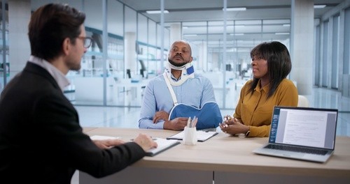 injured man wearing neck brace and arm sling meeting with attorney at desk