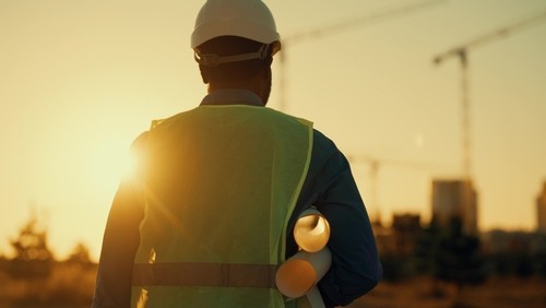 construction worker in hard hat and safety vest holding rolled blueprints on job site